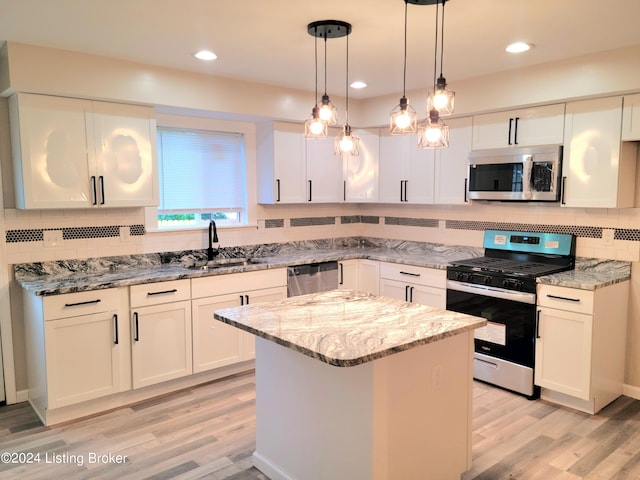 kitchen with hanging light fixtures, sink, white cabinetry, stainless steel appliances, and light wood-type flooring