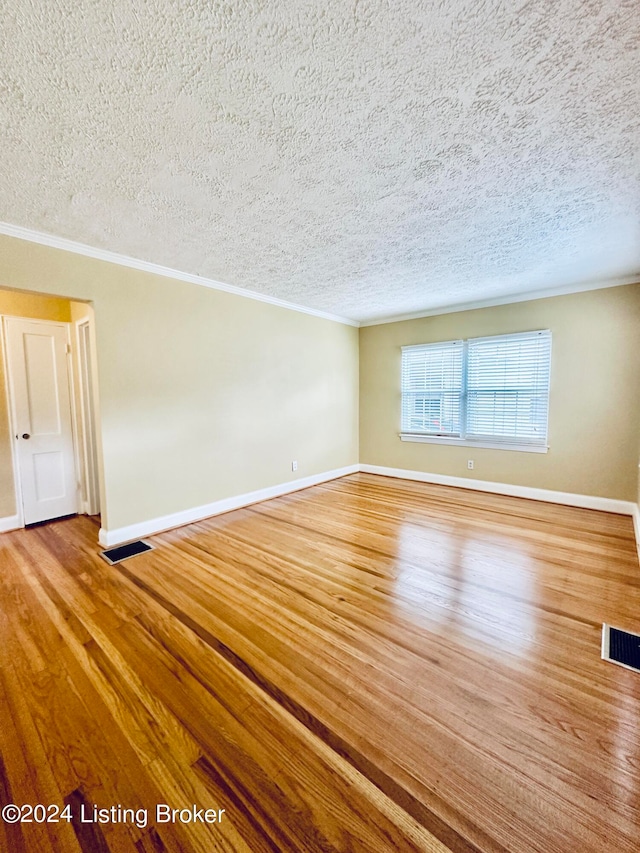 empty room with a textured ceiling, crown molding, and wood-type flooring