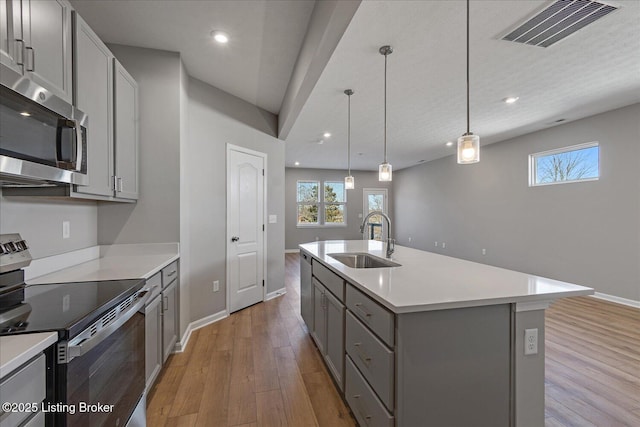 kitchen featuring sink, gray cabinetry, hanging light fixtures, a kitchen island with sink, and stainless steel appliances