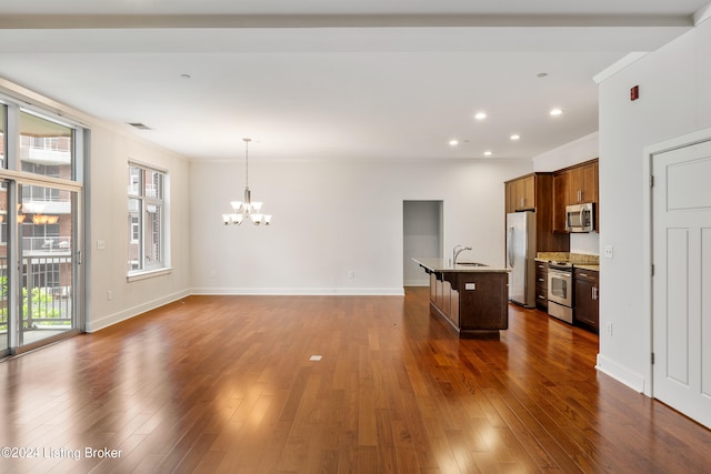 kitchen with dark hardwood / wood-style floors, an island with sink, stainless steel appliances, decorative light fixtures, and light stone counters