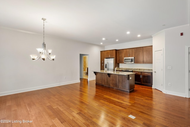 kitchen with decorative light fixtures, hardwood / wood-style floors, a center island with sink, and stainless steel appliances