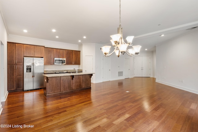 kitchen with an island with sink, stainless steel appliances, decorative light fixtures, wood-type flooring, and sink