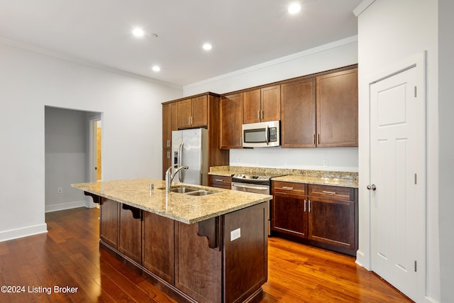 kitchen with light stone counters, stainless steel appliances, a kitchen island with sink, dark wood-type flooring, and sink