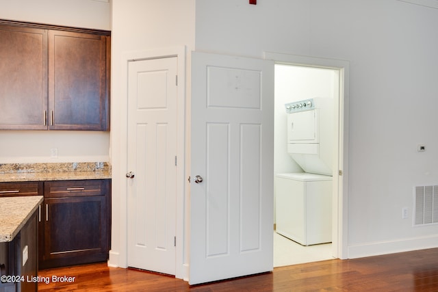 interior space featuring dark brown cabinetry, dark hardwood / wood-style flooring, stacked washer / drying machine, and light stone countertops