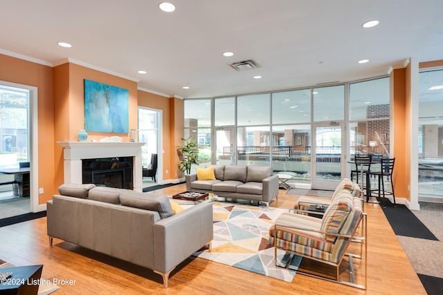 living room with a healthy amount of sunlight, expansive windows, ornamental molding, and light hardwood / wood-style floors