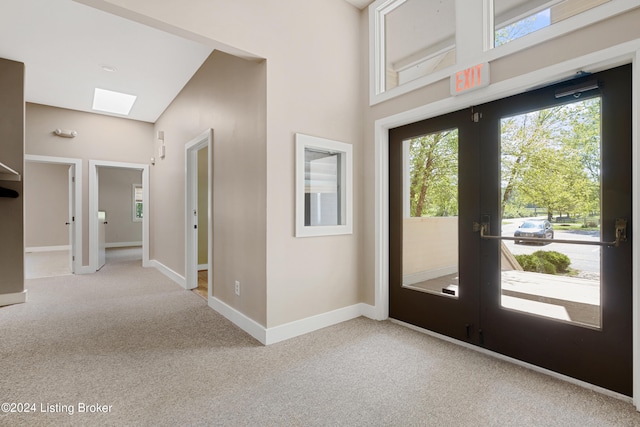 foyer featuring light carpet, a towering ceiling, french doors, and a skylight