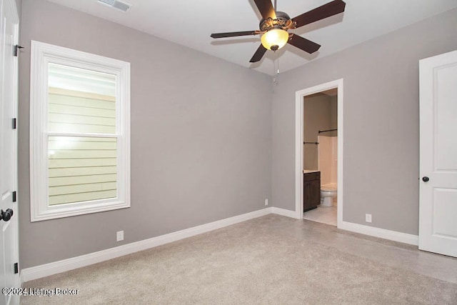 unfurnished bedroom featuring light colored carpet, ensuite bathroom, ceiling fan, and multiple windows