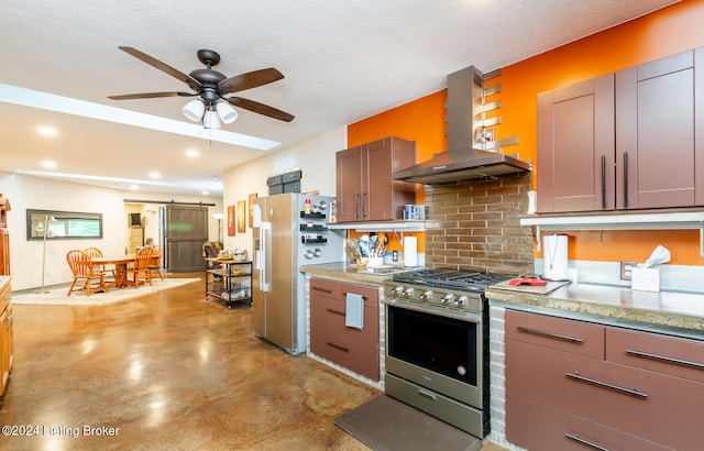 kitchen featuring wall chimney range hood, stainless steel range with gas stovetop, high end fridge, a barn door, and ceiling fan