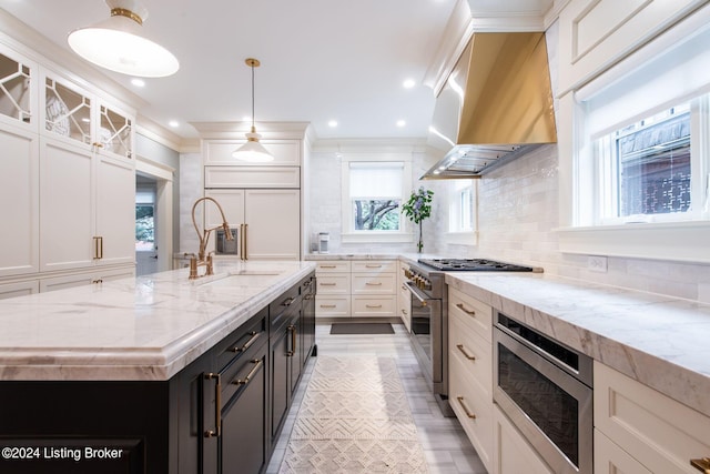 kitchen featuring built in appliances, light stone countertops, backsplash, a kitchen island with sink, and pendant lighting