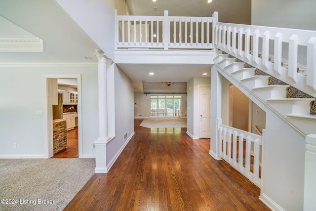 entrance foyer featuring ornate columns, crown molding, a high ceiling, and wood-type flooring