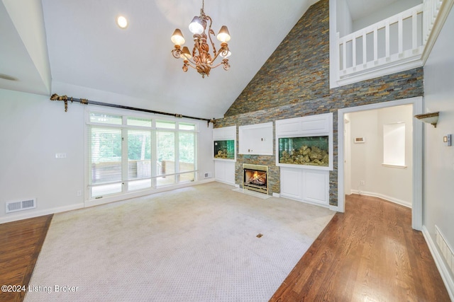 unfurnished living room featuring a fireplace, high vaulted ceiling, light hardwood / wood-style flooring, and an inviting chandelier