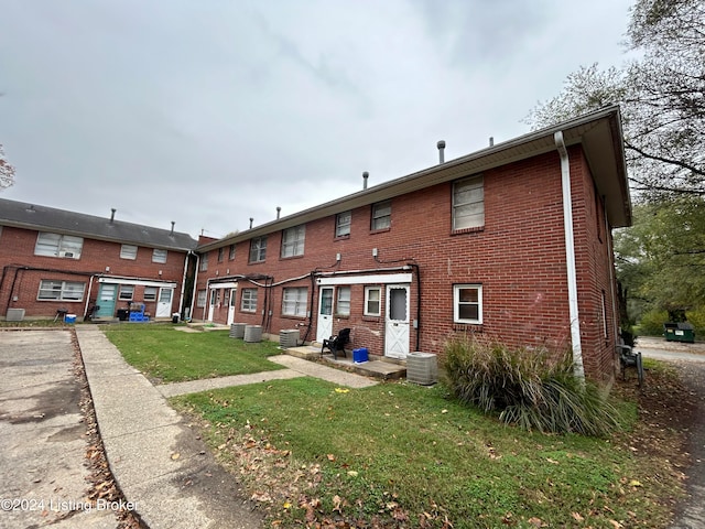 back of property with central AC unit and a lawn