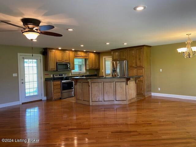 kitchen featuring appliances with stainless steel finishes, a center island, ceiling fan with notable chandelier, and hardwood / wood-style floors