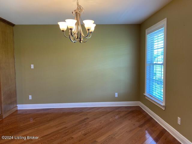 unfurnished room with a chandelier and dark wood-type flooring