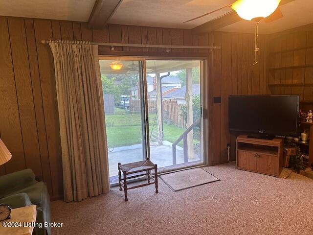 carpeted living room with beamed ceiling, a healthy amount of sunlight, and wooden walls