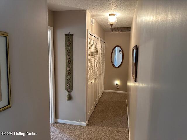 corridor with light colored carpet and a textured ceiling