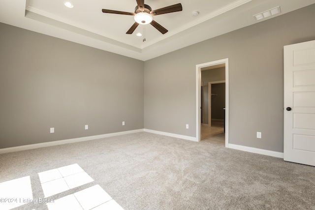 spare room with ceiling fan, light colored carpet, and a tray ceiling