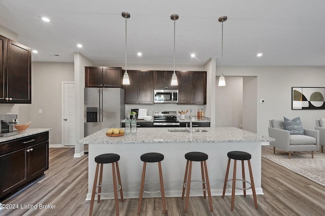 kitchen featuring a kitchen bar, stainless steel appliances, hardwood / wood-style flooring, and an island with sink