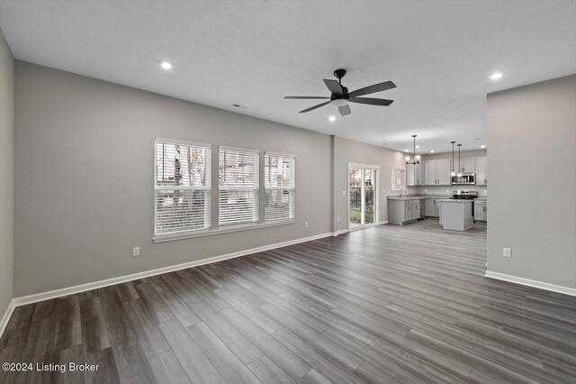 unfurnished living room featuring a textured ceiling, ceiling fan with notable chandelier, and dark wood-type flooring