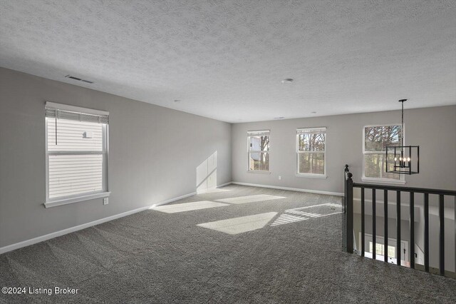 carpeted spare room with a textured ceiling and an inviting chandelier