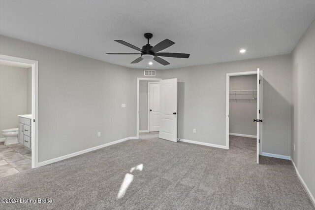 unfurnished bedroom with light carpet, ensuite bathroom, ceiling fan, a spacious closet, and a closet