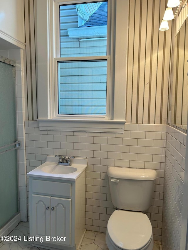 bathroom featuring vanity, a shower with door, tile walls, tile patterned flooring, and toilet