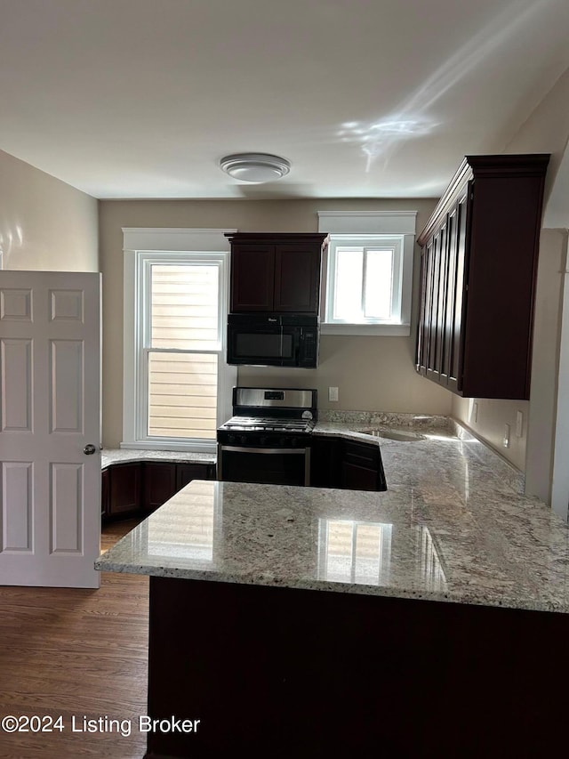 kitchen featuring hardwood / wood-style floors, dark brown cabinets, light stone counters, and stainless steel range with gas cooktop