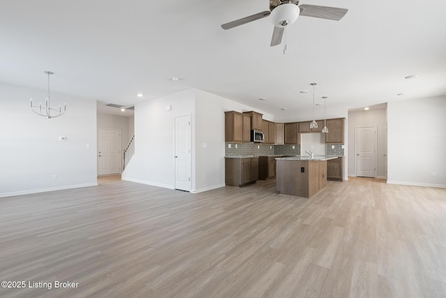 kitchen with a kitchen island with sink, ceiling fan with notable chandelier, hanging light fixtures, decorative backsplash, and light wood-type flooring