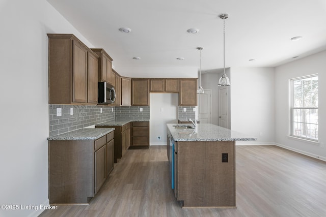 kitchen featuring light stone counters, sink, decorative light fixtures, a center island with sink, and light hardwood / wood-style floors