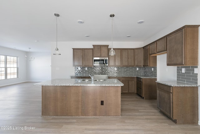 kitchen featuring hanging light fixtures, light stone counters, and a kitchen island with sink