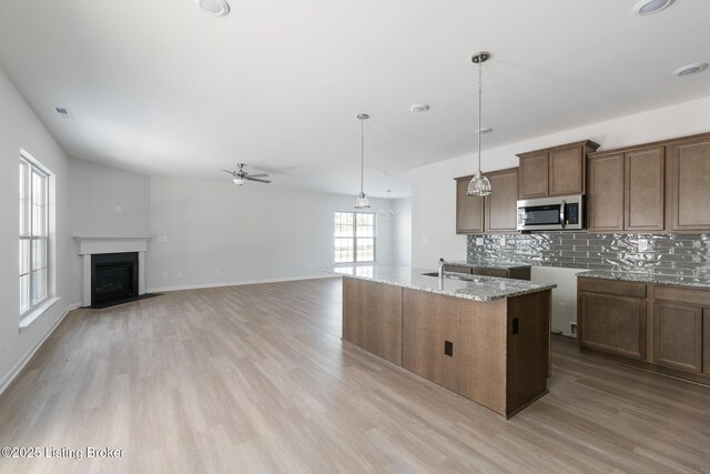 kitchen featuring light stone countertops, backsplash, ceiling fan, pendant lighting, and a center island with sink