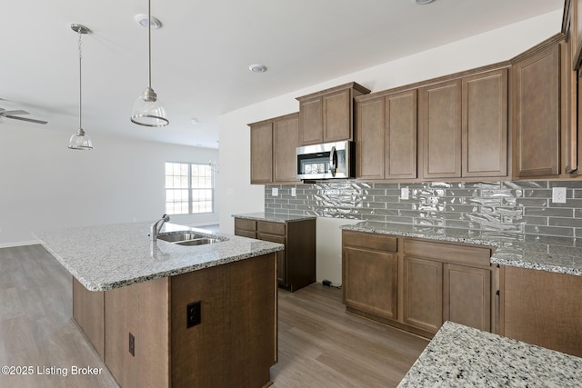 kitchen with decorative backsplash, decorative light fixtures, a kitchen island with sink, and sink