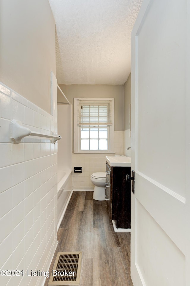 full bathroom with hardwood / wood-style floors, a textured ceiling, toilet, vanity, and tile walls