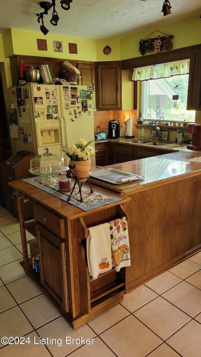 kitchen with sink, dark brown cabinets, white fridge with ice dispenser, a textured ceiling, and light tile patterned flooring