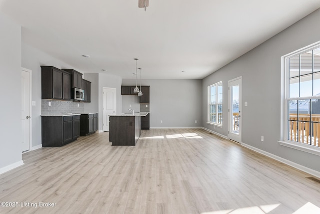 kitchen with sink, backsplash, light hardwood / wood-style floors, decorative light fixtures, and a kitchen island with sink