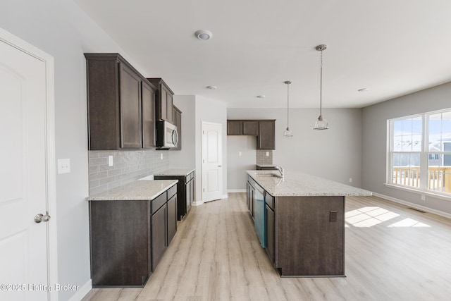 kitchen featuring decorative backsplash, light stone counters, a kitchen island with sink, sink, and pendant lighting