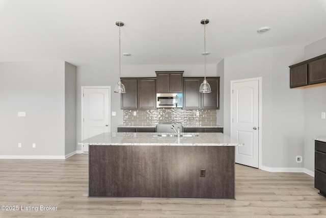 kitchen with decorative backsplash, dark brown cabinetry, a center island with sink, and sink