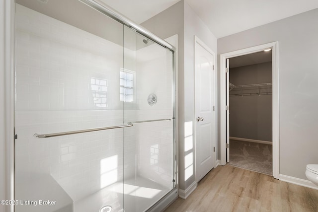 bathroom with hardwood / wood-style floors, toilet, and a shower with door