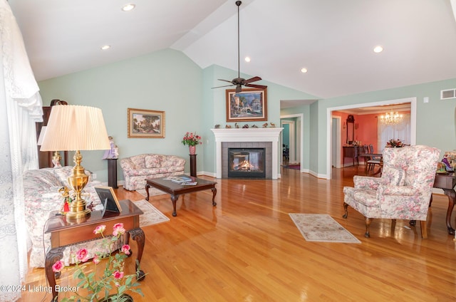 living room with lofted ceiling, a tiled fireplace, wood-type flooring, and ceiling fan with notable chandelier