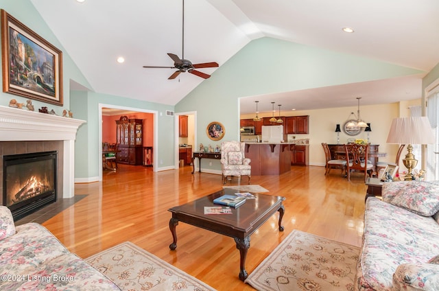 living room with a tile fireplace, high vaulted ceiling, ceiling fan, and light wood-type flooring