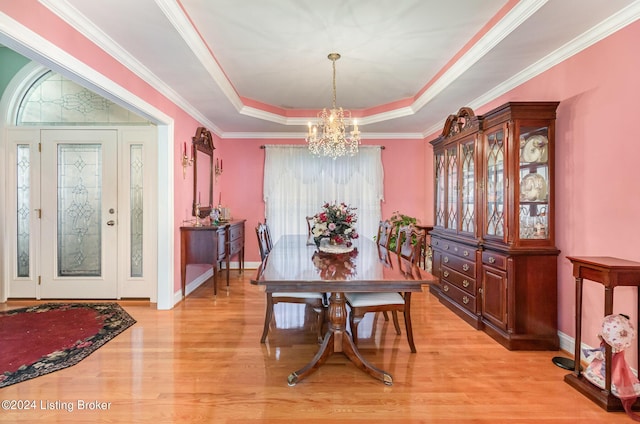 dining space with crown molding, a tray ceiling, a chandelier, and light wood-type flooring