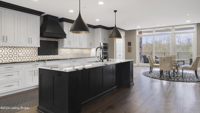 kitchen with pendant lighting, backsplash, premium range hood, a center island with sink, and dark hardwood / wood-style flooring