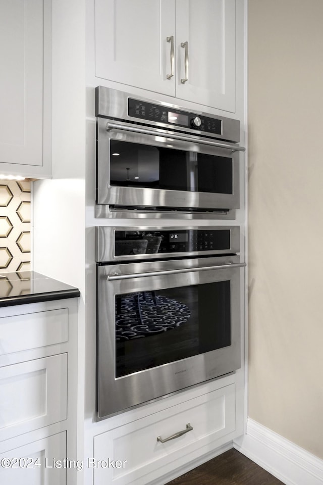 kitchen with stainless steel double oven, white cabinetry, and dark wood-type flooring