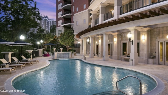 pool at dusk with a patio area, pool water feature, and elevator