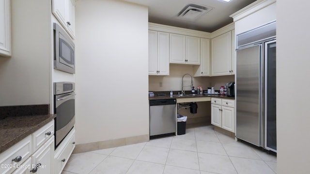 kitchen featuring light tile patterned floors, built in appliances, white cabinetry, and sink