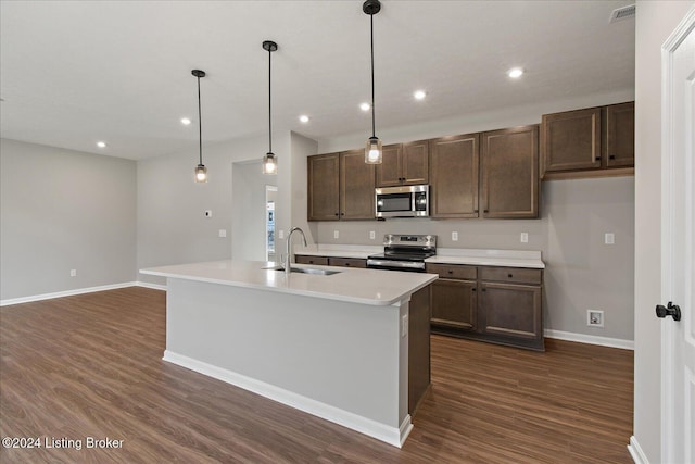 kitchen with pendant lighting, dark hardwood / wood-style flooring, stainless steel appliances, sink, and a kitchen island with sink