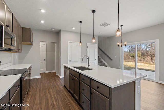 kitchen with an island with sink, appliances with stainless steel finishes, dark hardwood / wood-style floors, pendant lighting, and sink