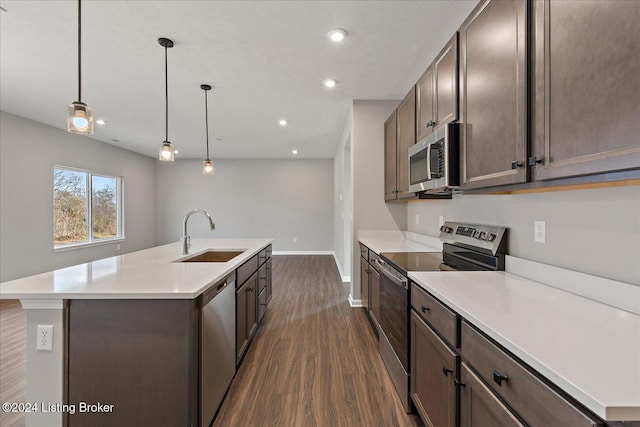 kitchen with decorative light fixtures, dark wood-type flooring, stainless steel appliances, sink, and a kitchen island with sink