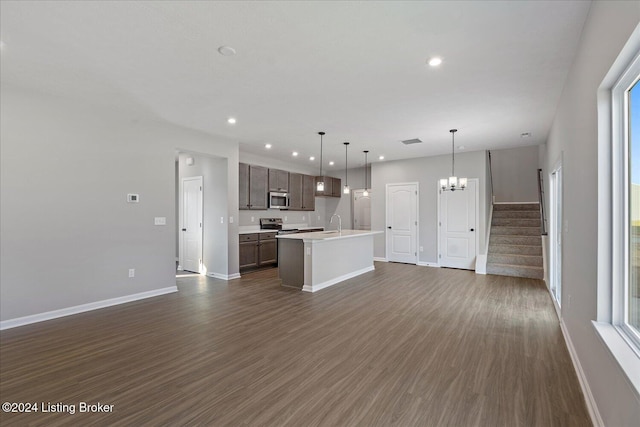 kitchen with decorative light fixtures, dark wood-type flooring, stainless steel appliances, an island with sink, and dark brown cabinets