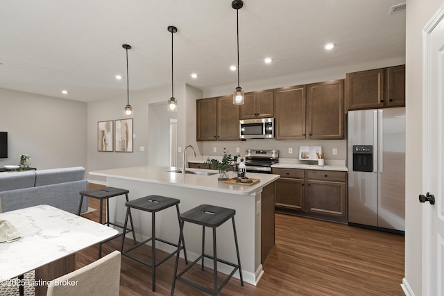 kitchen featuring an island with sink, stainless steel appliances, decorative light fixtures, a breakfast bar, and sink